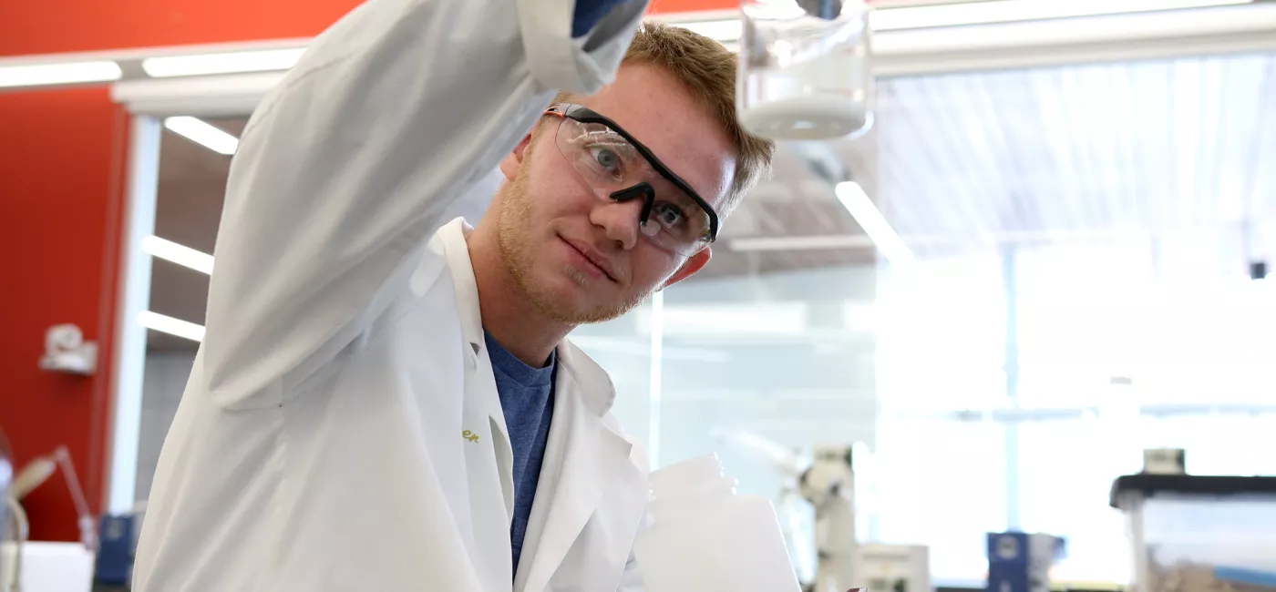 A student in goggles examines a jar in a lab